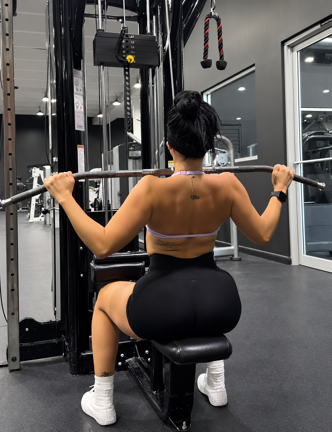 Ariana M. Thompson seated at a cable machine performing a wide-grip lat pulldown