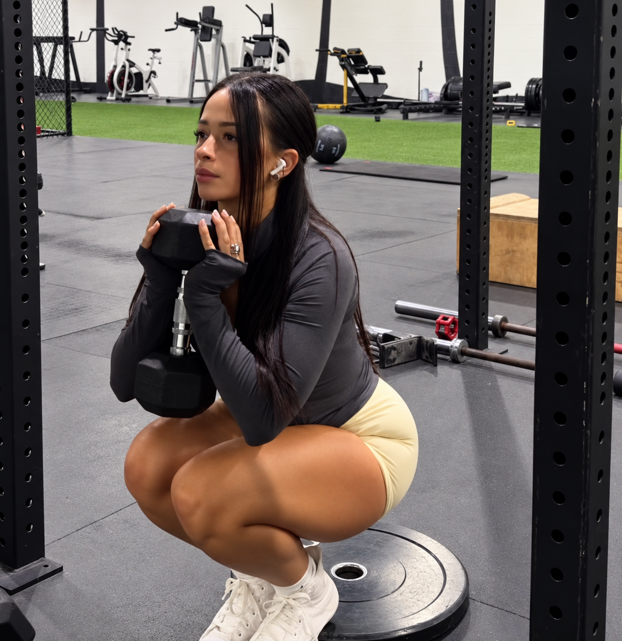 Ariana M. Thompson performing a goblet squat with a dumbbell in a gym rack
