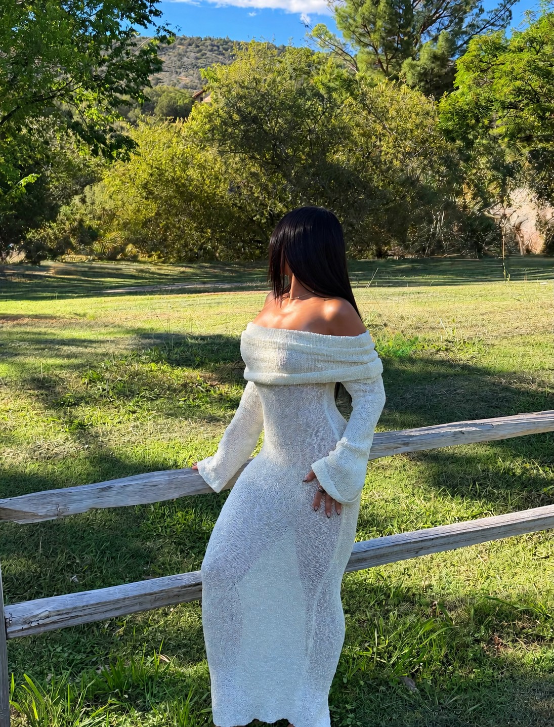 Ariana M. Thompson wearing a white knit dress beside an outdoor wooden fence