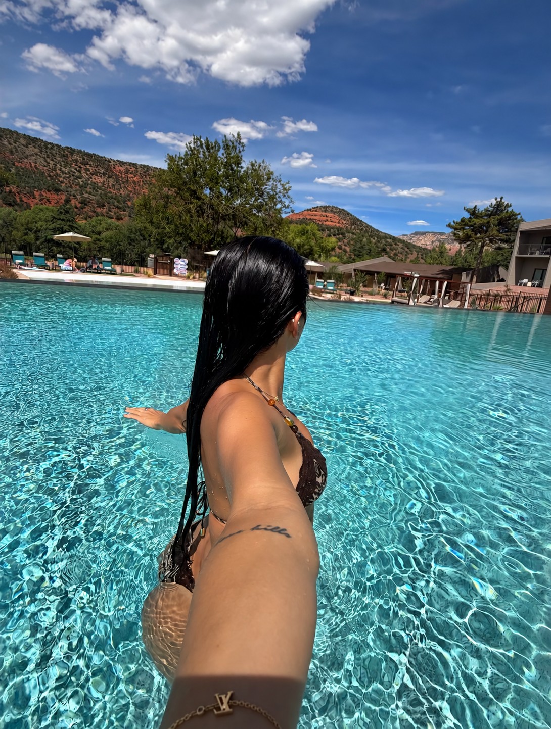 Ariana M. Thompson taking a poolside selfie with water and hills behind her